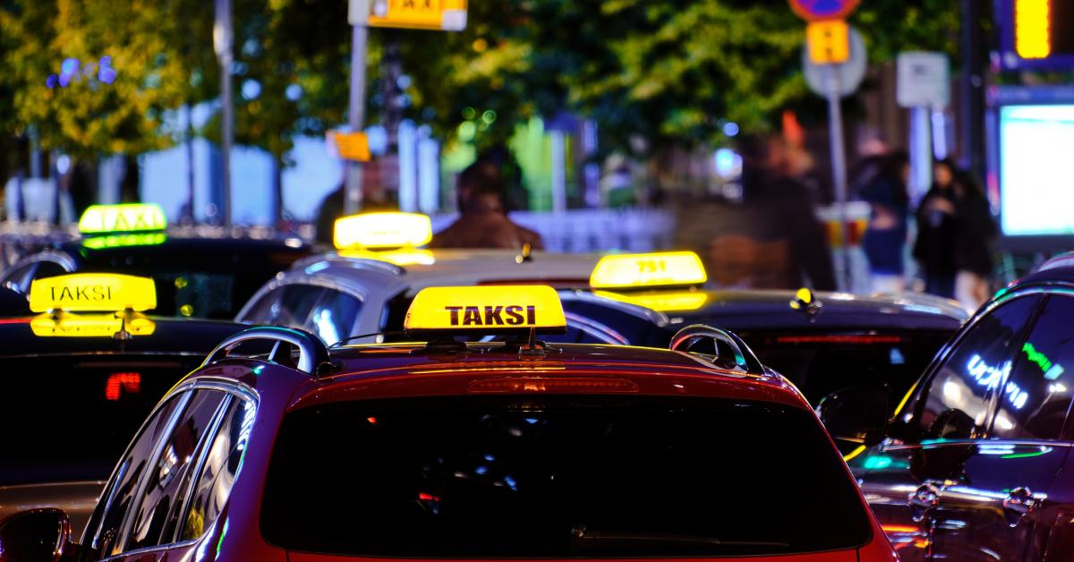 Sex taxibilar vid en taxistation i skymningen.