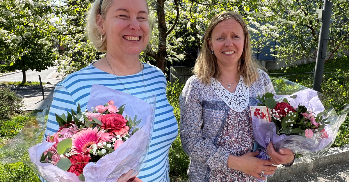 Tessa Bamberg och Stina Nygård står glada med blombuketter i händerna. I bakgrunden träd med vita blommor.