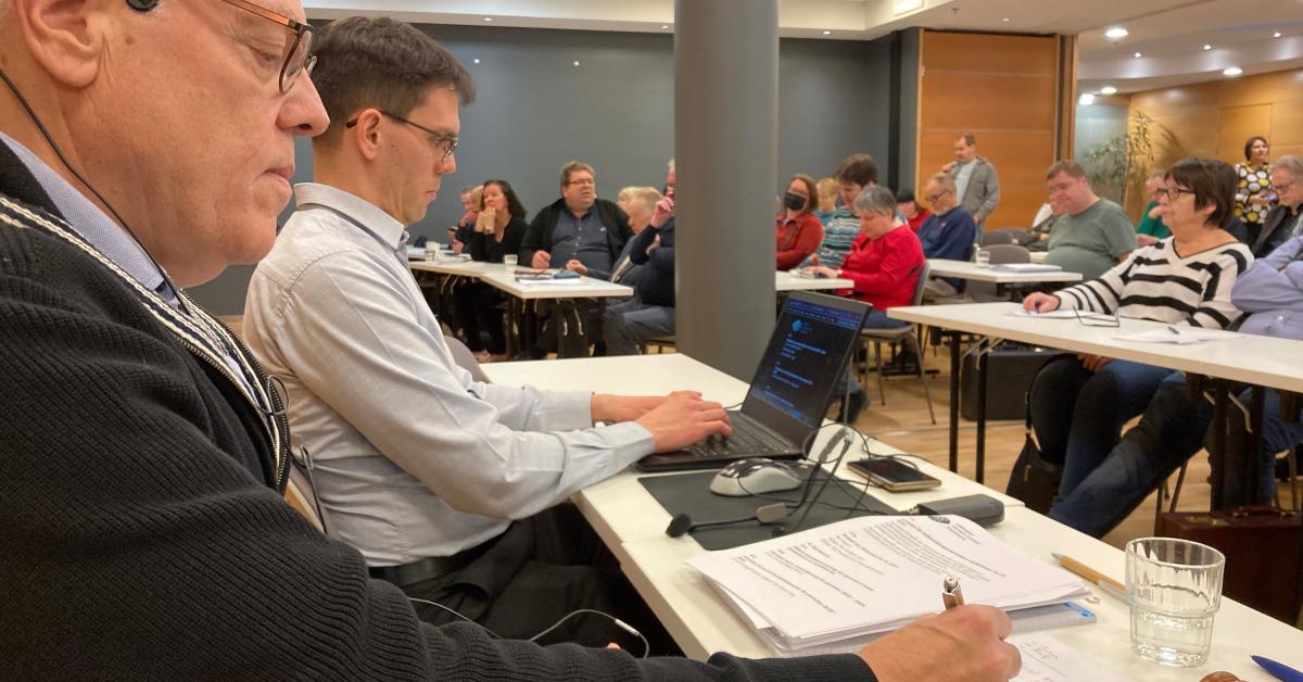 I förgrunden mötesordförande Stefan Andersson och verksamhetsledare Matthias Jakobsson. I salen sitter medlemmar vid långsmala bord och i bakgrunden syns Johan Sundholm som talar i en mikrofon. 