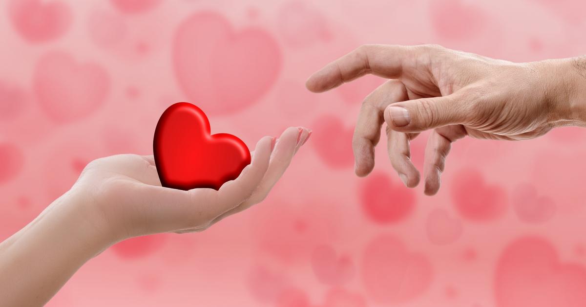 En hand räcker ett ritat hjärta till en annan hand. Röd bakgrund med svävande hjärtor.