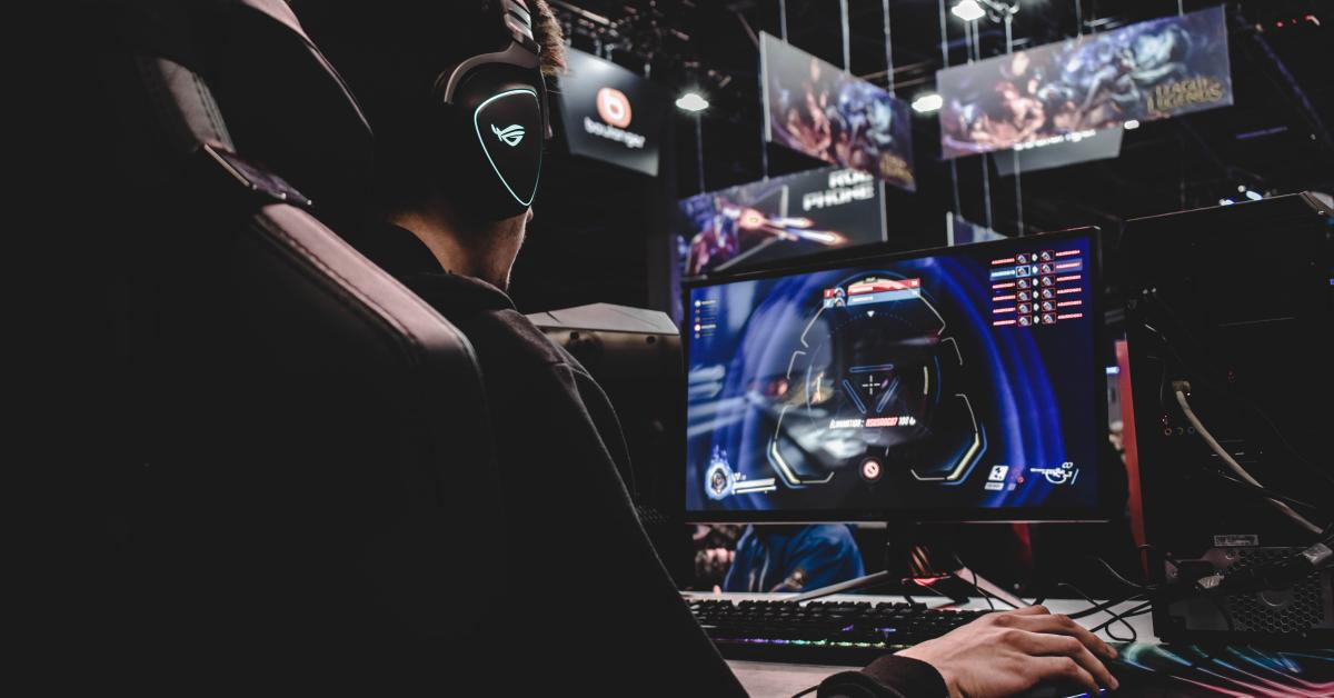 Ung man med hörlurar spelar datorspel framför stora skärmar.