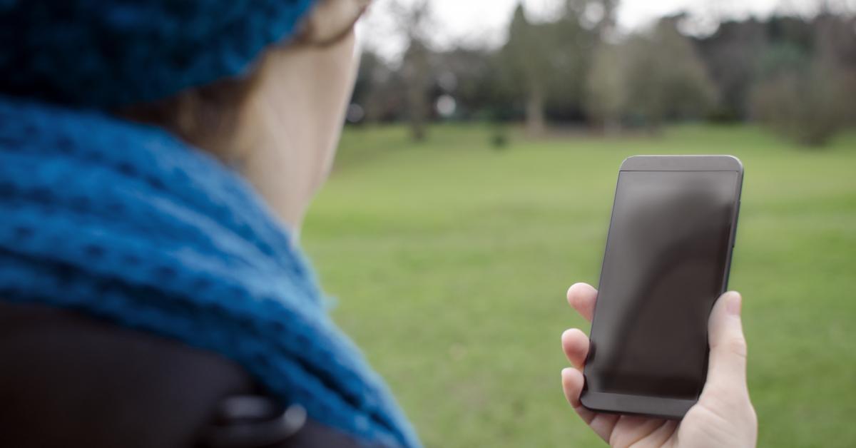 Dam utomhus med smarttelefon i handen.
