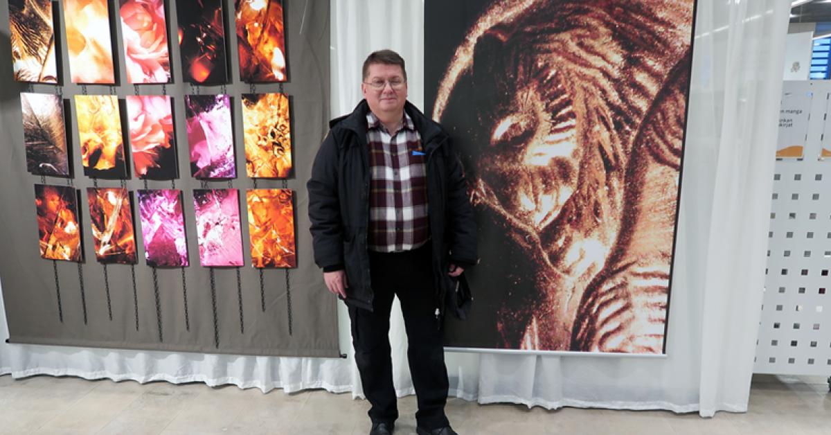Tero Kokko, man i äldre medelåldern, stor leende vid väggen med färggranna fototavlor.