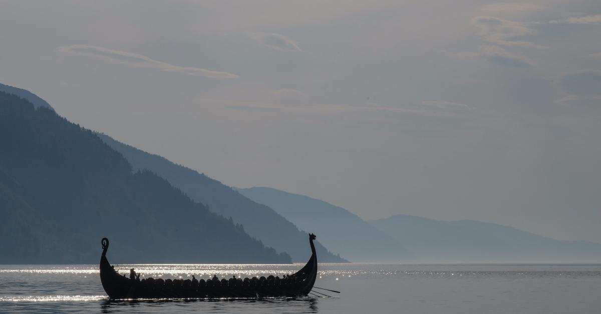 Ett enkelt vikingaskepp i vattnet. I bakgrunden ett berg eller en fjord.