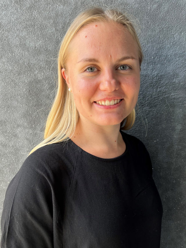 Elin har långt blont hår med mittbena, ler och är klädd i en svart skjorta.