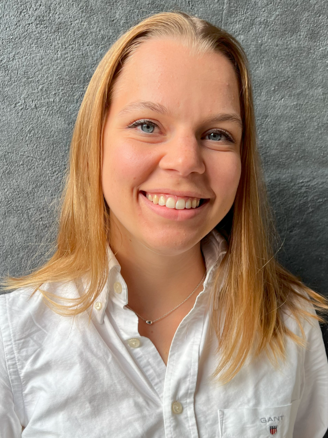 Halvfigur av en ung kvinna med blå ögon och blont, rakt hår, lite över axellängd.  Hon är klädd i en vit skjorta och ser glad ut.